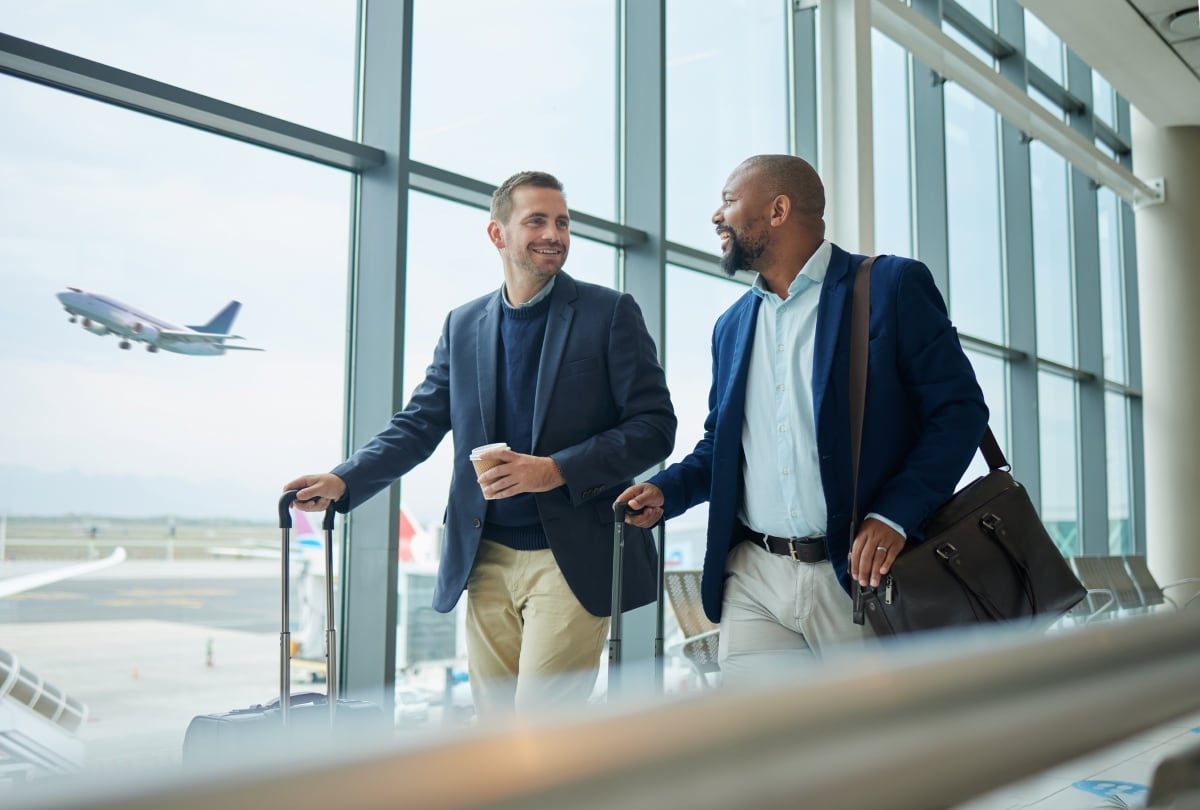 Zwei männliche Geschäftsreisende mit Rollkoffern am Flughafen als Symbol für rechtssichere Compliance und automatisierte A1-Bescheinigungen bei Auslandsdienstreisen.