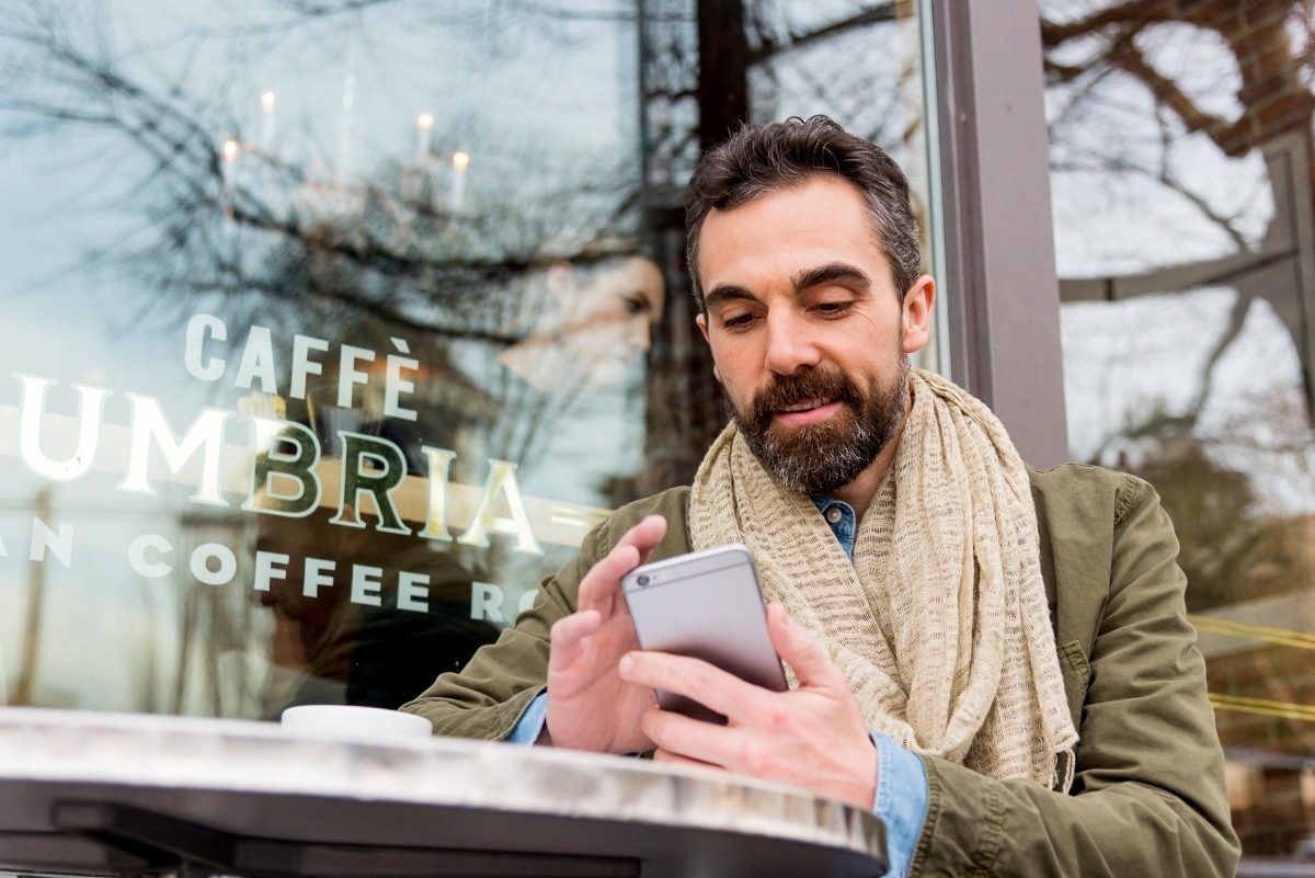 Ein Mann sitzt mit seinem Handy in einem Café und nutzt die ExpenseIt-Funktion der mobilen App zur digitalen Belegerfassung.