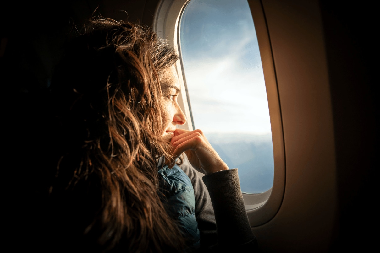 Eine Geschäftsreisende blickt während eines Business-Flugs aus dem Flugzeugfenster und bereitet sich auf ihren nächsten Kundentermin vor.
