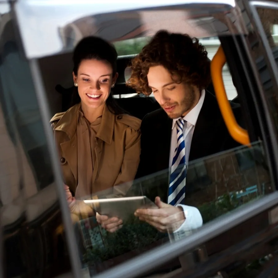 Eine Frau und ein Mann sitzen entspannt im Auto und blicken auf ein Tablet – als Symbolbild für den Weg zum KI-gestützten, autonomen Geschäftsreiseprozess.