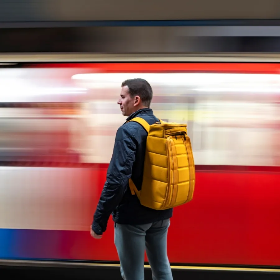Geschäftsreisender mit Rucksack steht mit dem Rücken zur Kamera vor einer fahrenden U-Bahn.