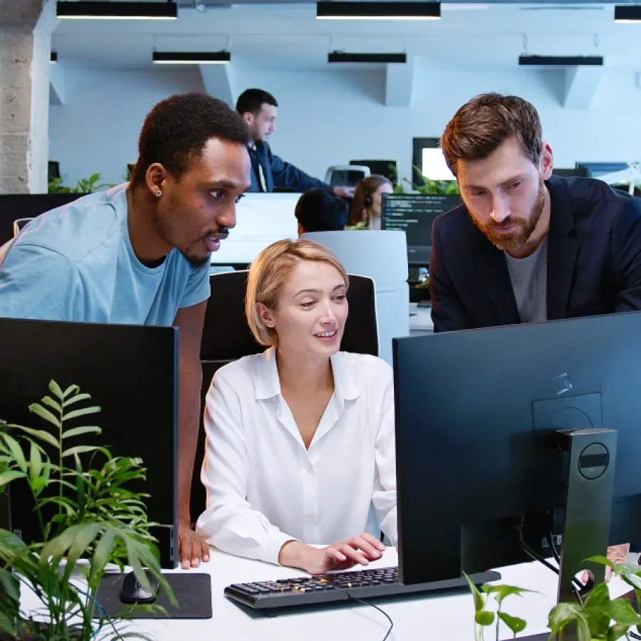 Ein diverses Team von Kolleginnen und Kollegen bespricht gemeinsam ein Projekt an einem Computer in einem modernen Büroraum.